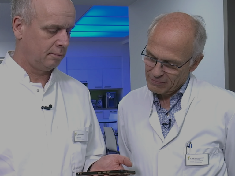 Dr. Hans-Josef Lemmen und Dr. Marko Böhm blicken im Krankenhausflur auf ein Smartphone im Immanuel Universitätsklinik Rüdersdorf